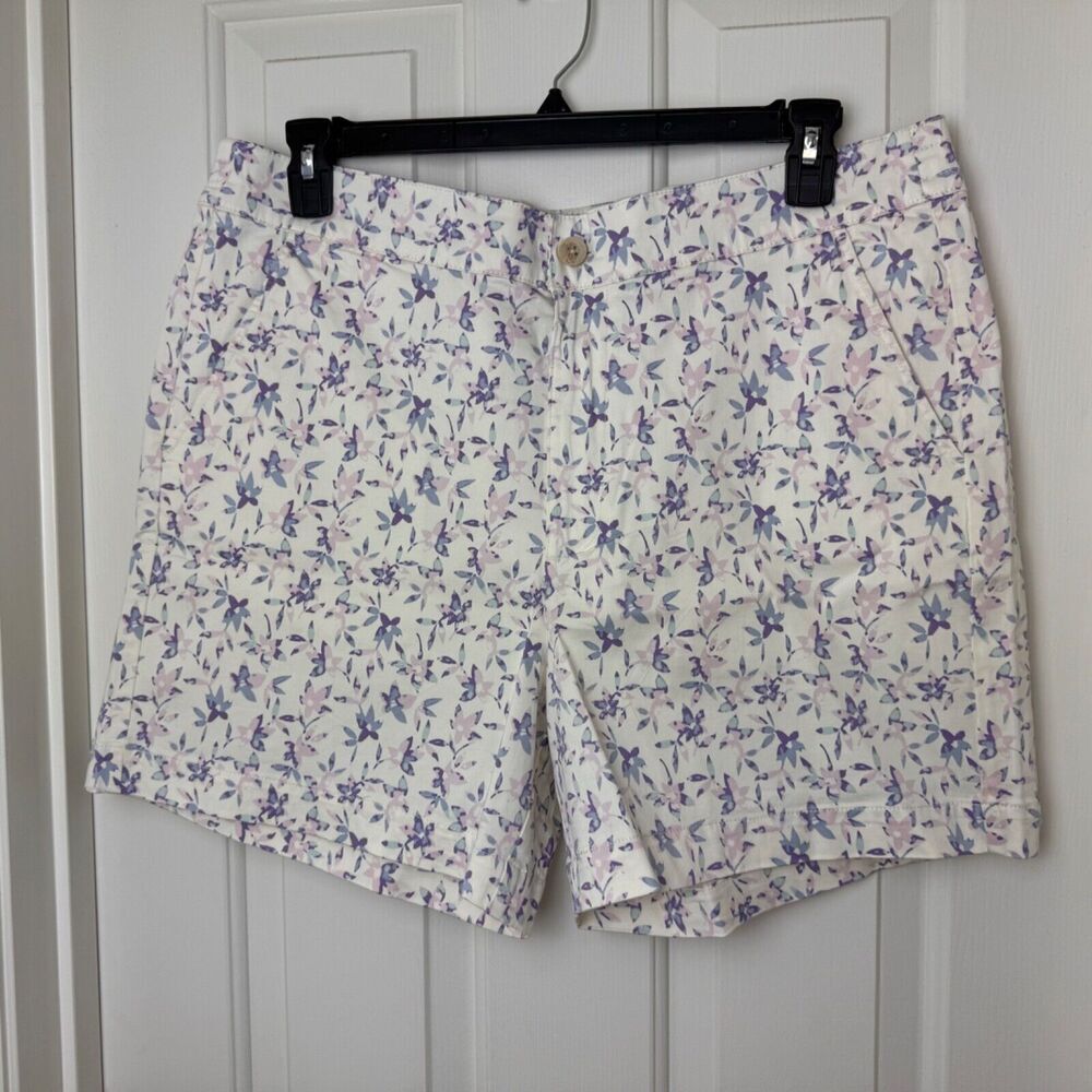 White shorts with a purple and pink floral print, hanging on a black hanger against a white paneled door.