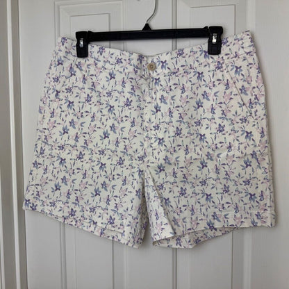 White shorts with a purple and pink floral print, hanging on a black hanger against a white paneled door.