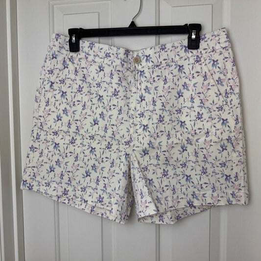 White shorts with a purple and pink floral print, hanging on a black hanger against a white paneled door.