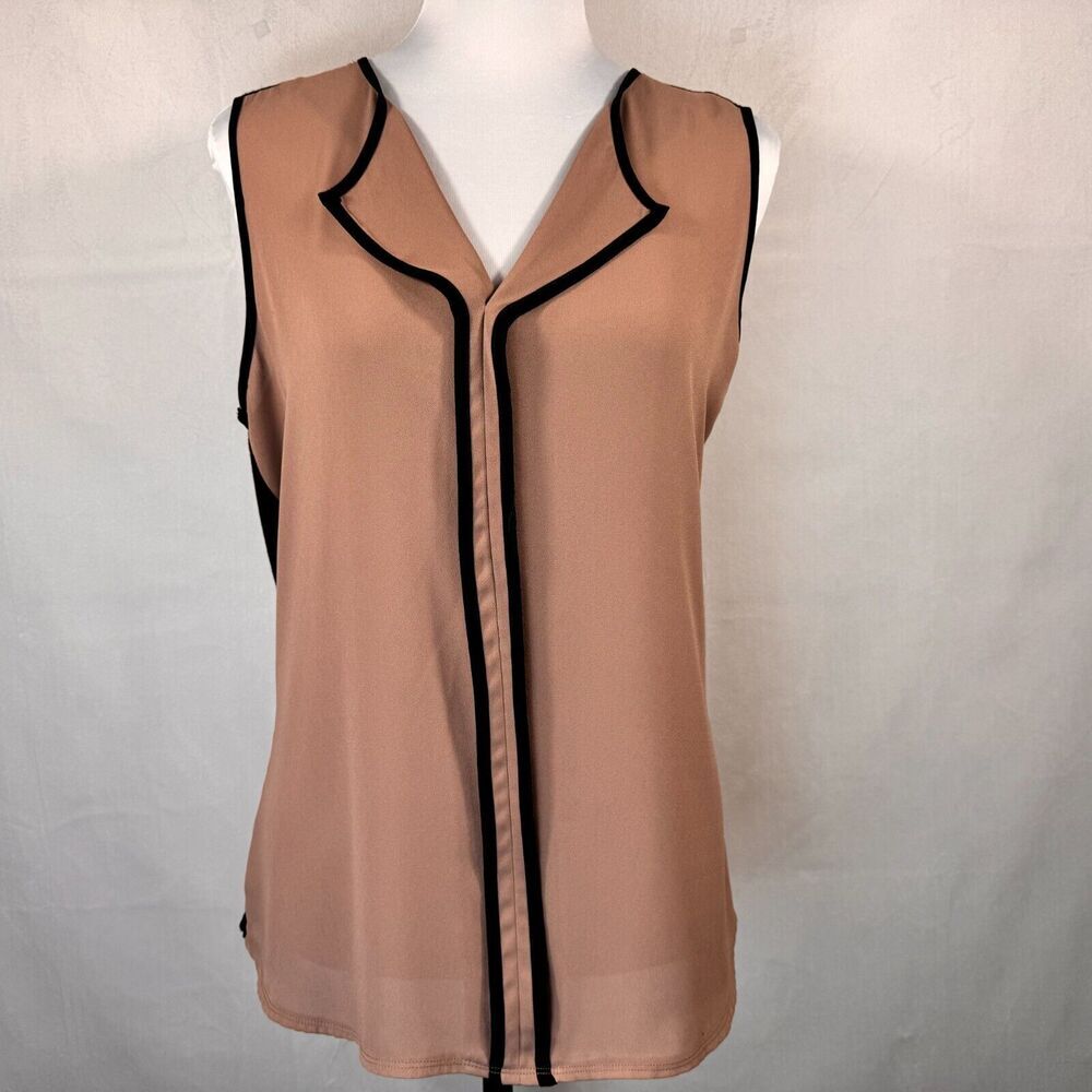 A sleeveless beige blouse with black piping trim, displayed on a white mannequin torso against a light gray fabric backdrop.