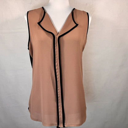 A sleeveless beige blouse with black piping trim, displayed on a white mannequin torso against a light gray fabric backdrop.