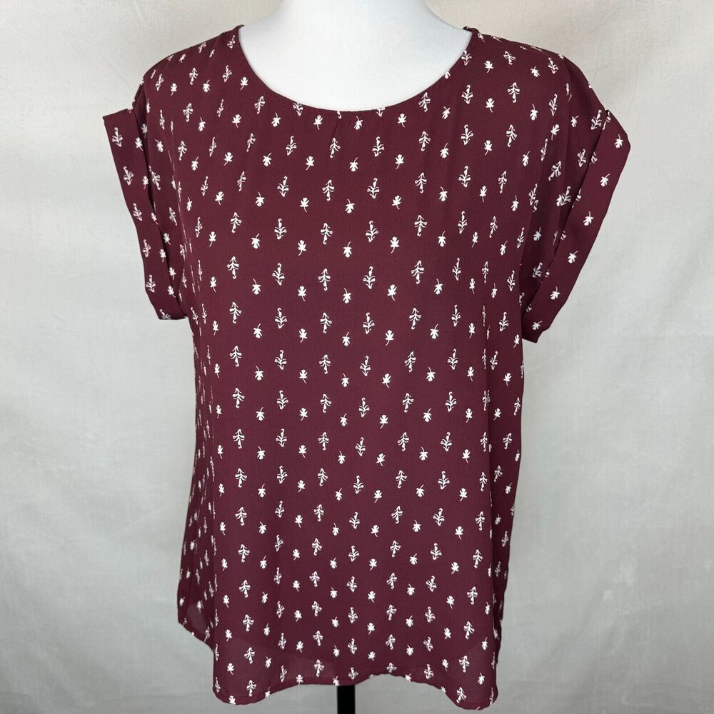 A women's short-sleeve top in burgundy with a white allover floral pattern, displayed on a white mannequin torso against a light gray fabric backdrop.
