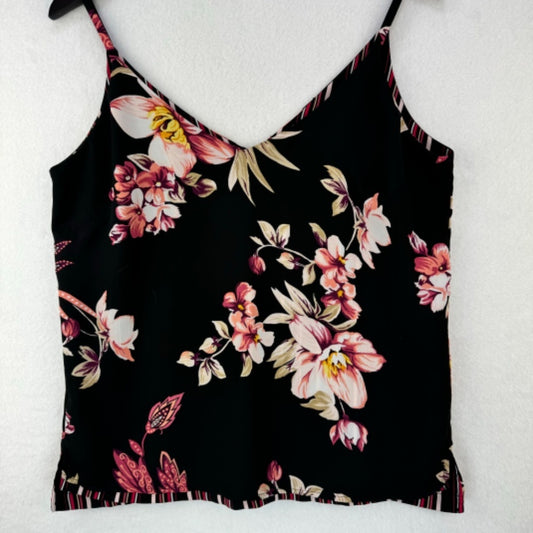 A black camisole tank top with a vibrant floral print in pink, white, and beige, featuring thin spaghetti straps and a ruffled hem, displayed on a white textured background.