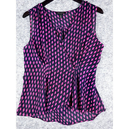 A sleeveless wrap-style blouse with a vibrant pink and black geometric pattern, hanging on a black hanger against a textured gray background.