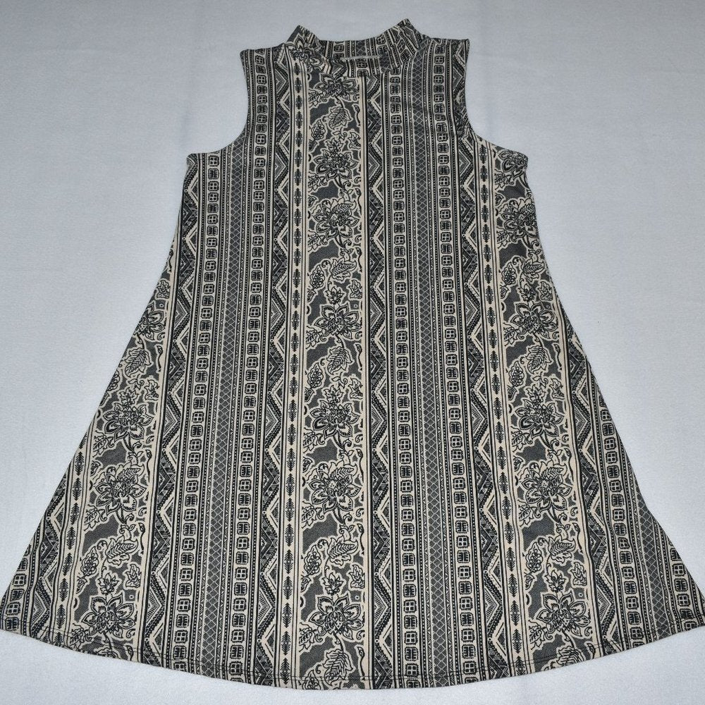 A sleeveless A-line dress with a high mock neck, featuring a vertical tribal and floral pattern in black and beige on a light gray background.