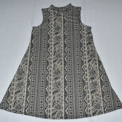A sleeveless A-line dress with a high mock neck, featuring a vertical tribal and floral pattern in black and beige on a light gray background.