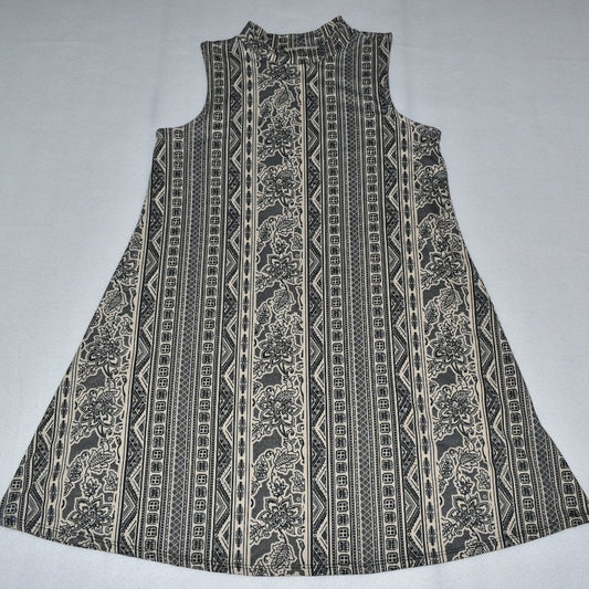 A sleeveless A-line dress with a high mock neck, featuring a vertical tribal and floral pattern in black and beige on a light gray background.