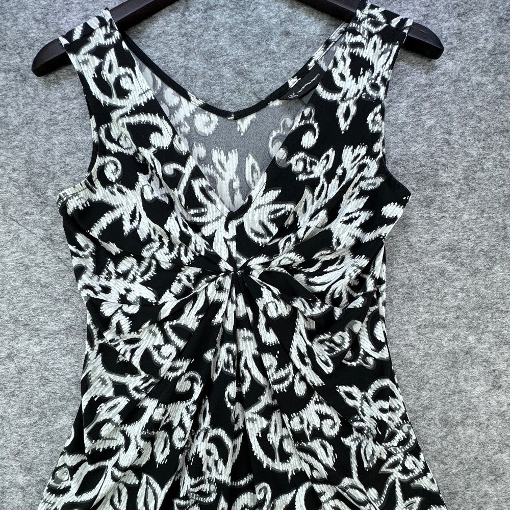 Black and white floral print sleeveless dress with a V-neckline and front twist detail, hanging on a black hanger against a gray felt background.