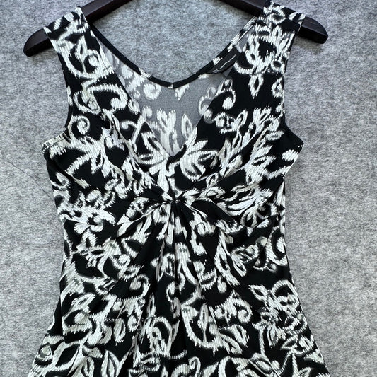 Black and white floral print sleeveless dress with a V-neckline and front twist detail, hanging on a black hanger against a gray felt background.