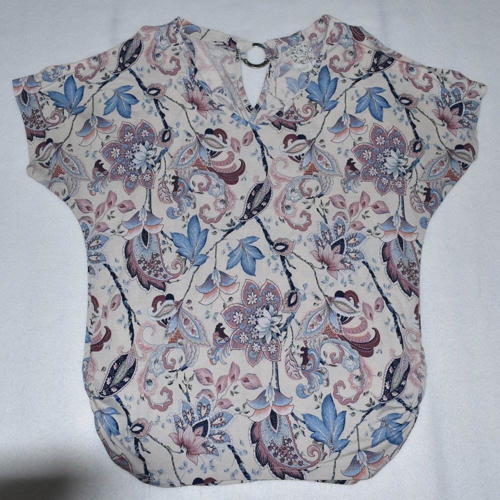 A short-sleeve blouse with a V-neckline, featuring an intricate floral and paisley pattern in shades of blue, pink, and brown on a light beige background.