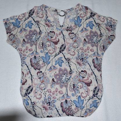 A short-sleeve blouse with a V-neckline, featuring an intricate floral and paisley pattern in shades of blue, pink, and brown on a light beige background.