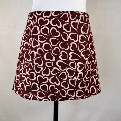 A high-waisted A-line mini skirt with an all-over repeating heart pattern in dark burgundy and cream, displayed on a white mannequin torso.