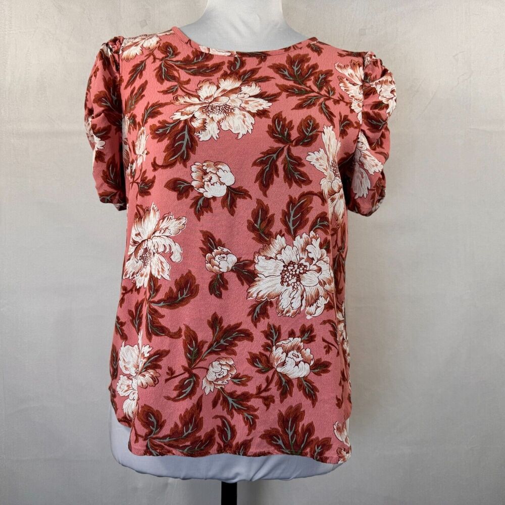 A dusty rose pink short-sleeve blouse with a white and dark red floral print, displayed on a mannequin torso against a light gray textured background.