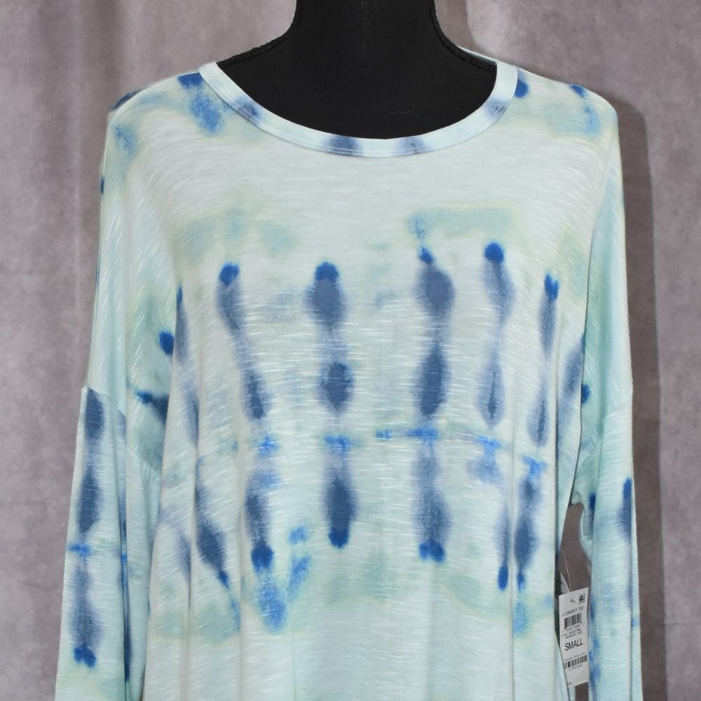 A long-sleeve tie-dye top displayed on a black mannequin torso against a textured gray backdrop. The top features a light mint green and white base with vertical blue tie-dye patterns.