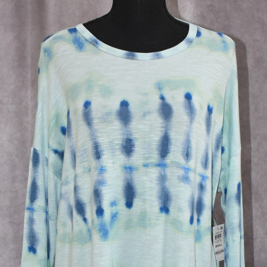 A long-sleeve tie-dye top displayed on a black mannequin torso against a textured gray backdrop. The top features a light mint green and white base with vertical blue tie-dye patterns.