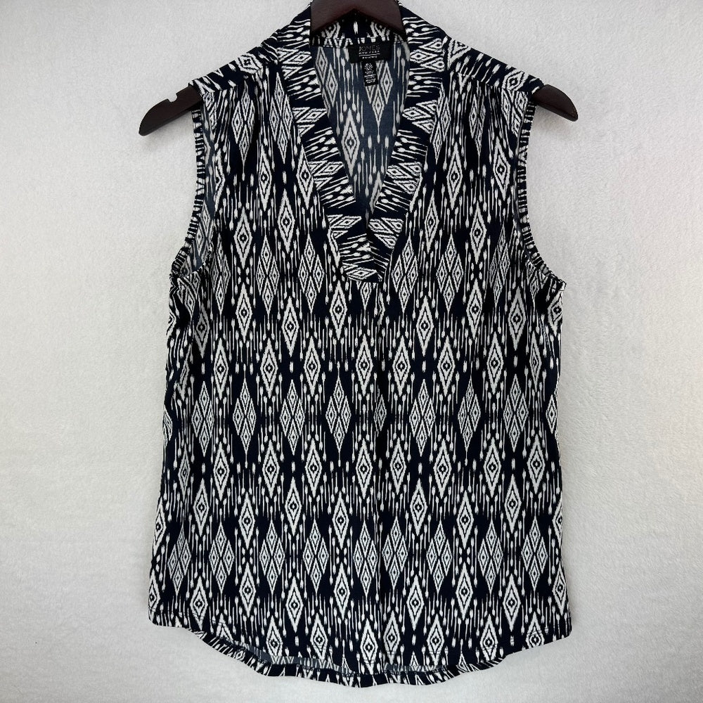 A sleeveless V-neck top with a black and white ikat diamond pattern, hanging on a dark wooden hanger against a textured off-white wall.