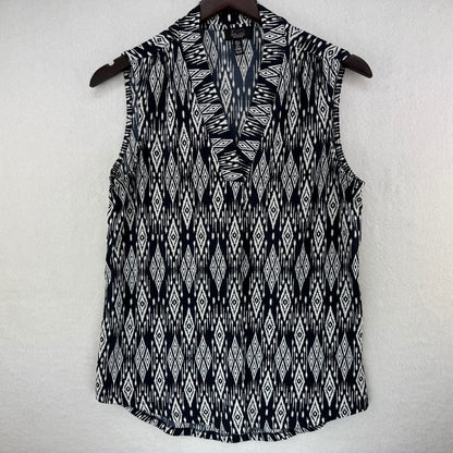 A sleeveless V-neck top with a black and white ikat diamond pattern, hanging on a dark wooden hanger against a textured off-white wall.