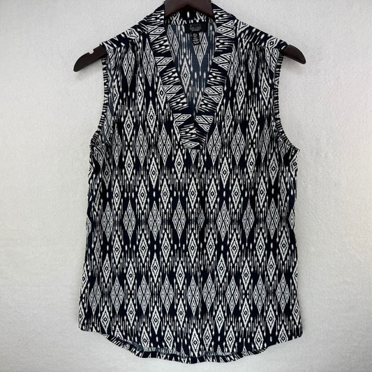 A sleeveless V-neck top with a black and white ikat diamond pattern, hanging on a dark wooden hanger against a textured off-white wall.