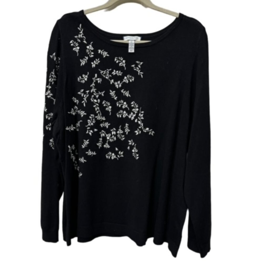 A black long-sleeve knit top with white floral embroidery on the front and left sleeve, hanging on a wooden hanger against a white background.