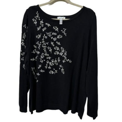 A black long-sleeve knit top with white floral embroidery on the front and left sleeve, hanging on a wooden hanger against a white background.