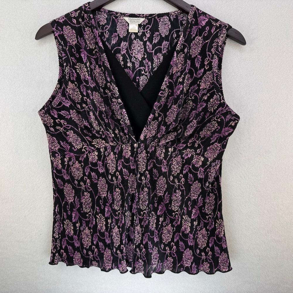 A sleeveless V-neck blouse with a black and purple floral pattern, hanging on a dark wooden hanger against a light gray textured wall.