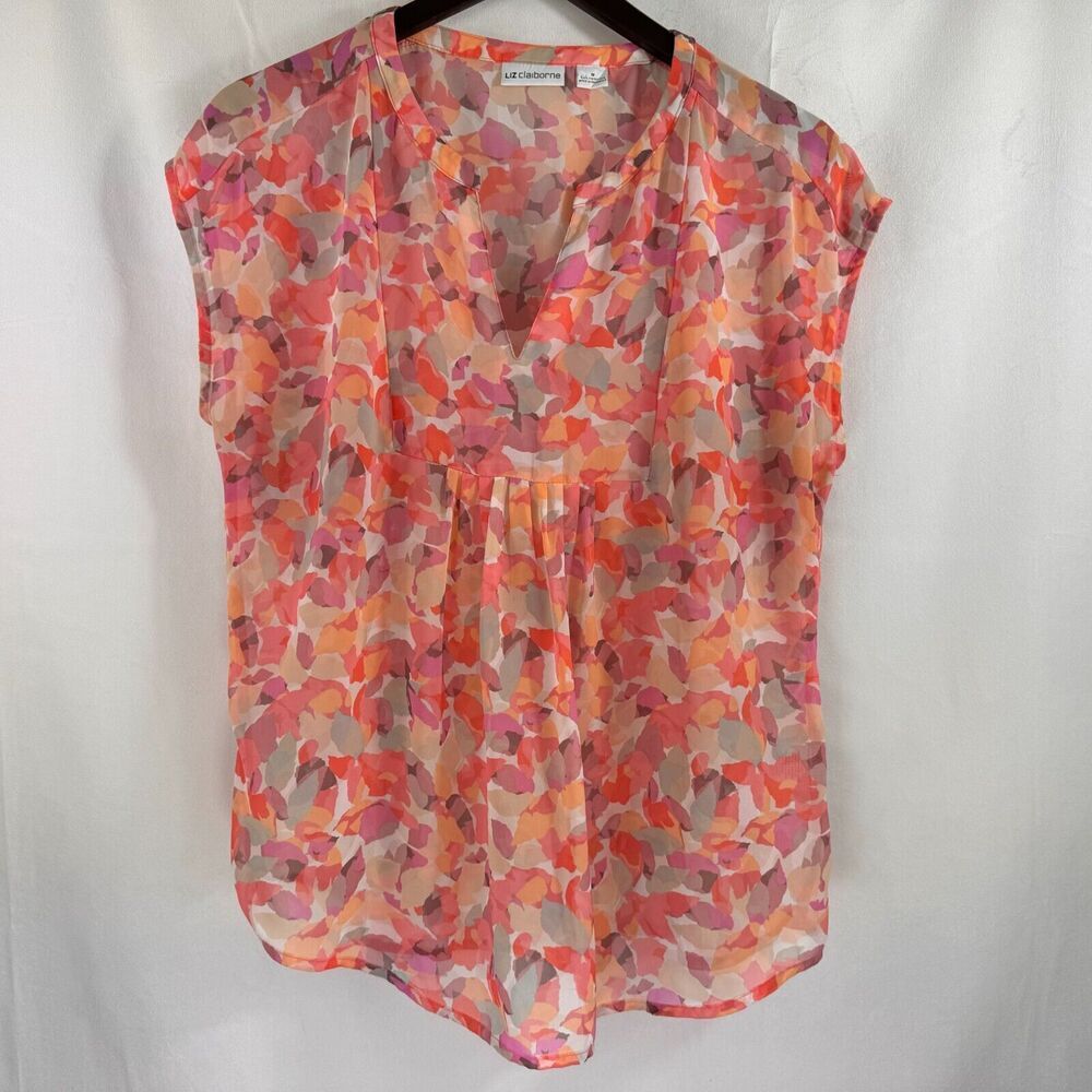 A sleeveless V-neck blouse with an abstract watercolor floral pattern in orange, pink, and beige, hanging on a black hanger against a white fabric backdrop.