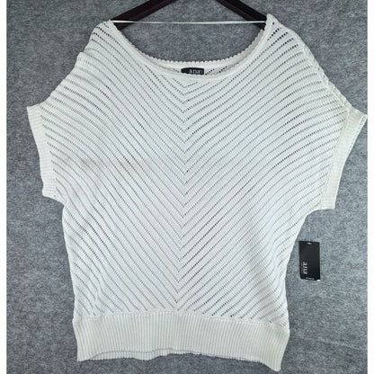 An off-white knit sweater with a chevron pattern and batwing sleeves, hanging on a dark hanger against a gray textured background. A black tag is visible on the right side.