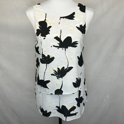 A sleeveless white top with a black floral print and small yellow speckles, displayed on a white mannequin torso against a light gray fabric backdrop.