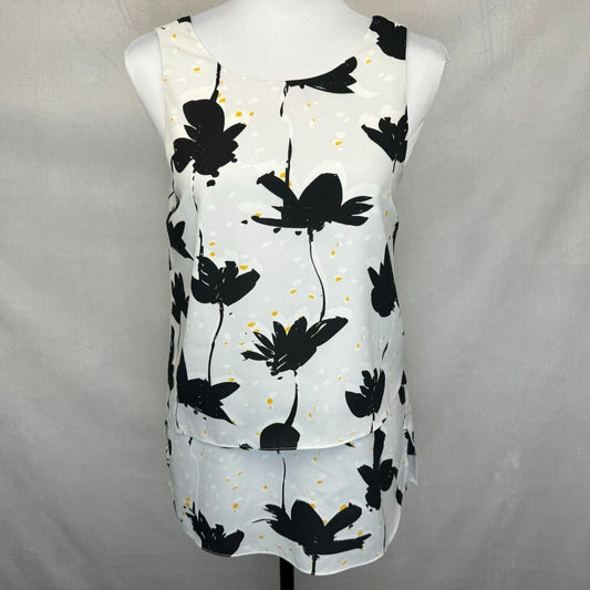 A sleeveless white top with a black floral print and small yellow speckles, displayed on a white mannequin torso against a light gray fabric backdrop.