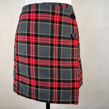 A plaid mini skirt in red, black, and gray with thin yellow stripes, displayed on a mannequin torso against a light gray fabric backdrop.