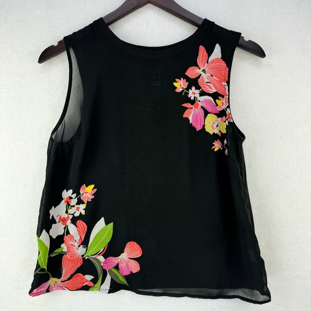 A black sleeveless mesh top with vibrant pink, red, green, and white floral embroidery, hanging on a dark wooden hanger against a light textured wall.