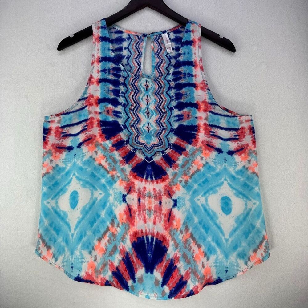 A sleeveless tank top with a vibrant blue, red, and white tie-dye pattern, hanging on a black hanger against a light gray textured wall.
