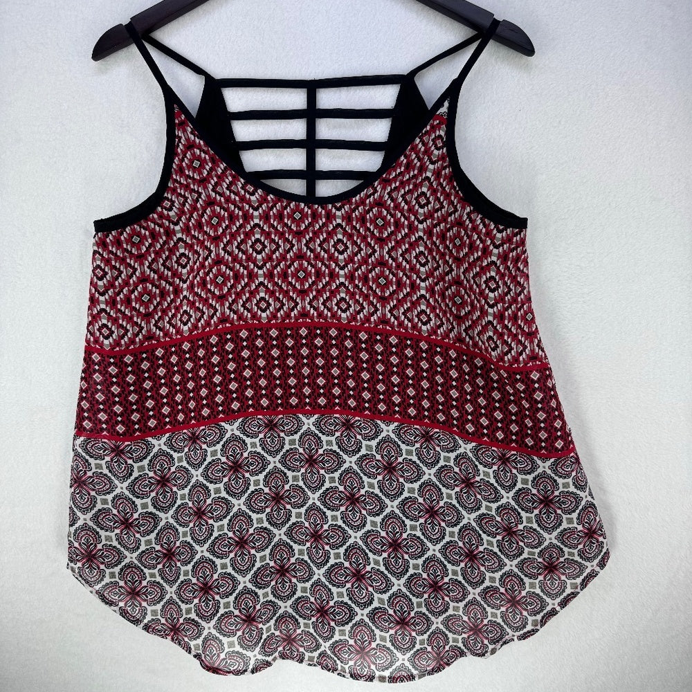 A sleeveless patterned camisole top hanging on a black hanger against a light gray wall. The top features a red, black, and white geometric and floral pattern, with black strappy details at the back.