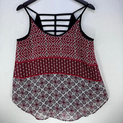 A sleeveless patterned camisole top hanging on a black hanger against a light gray wall. The top features a red, black, and white geometric and floral pattern, with black strappy details at the back.