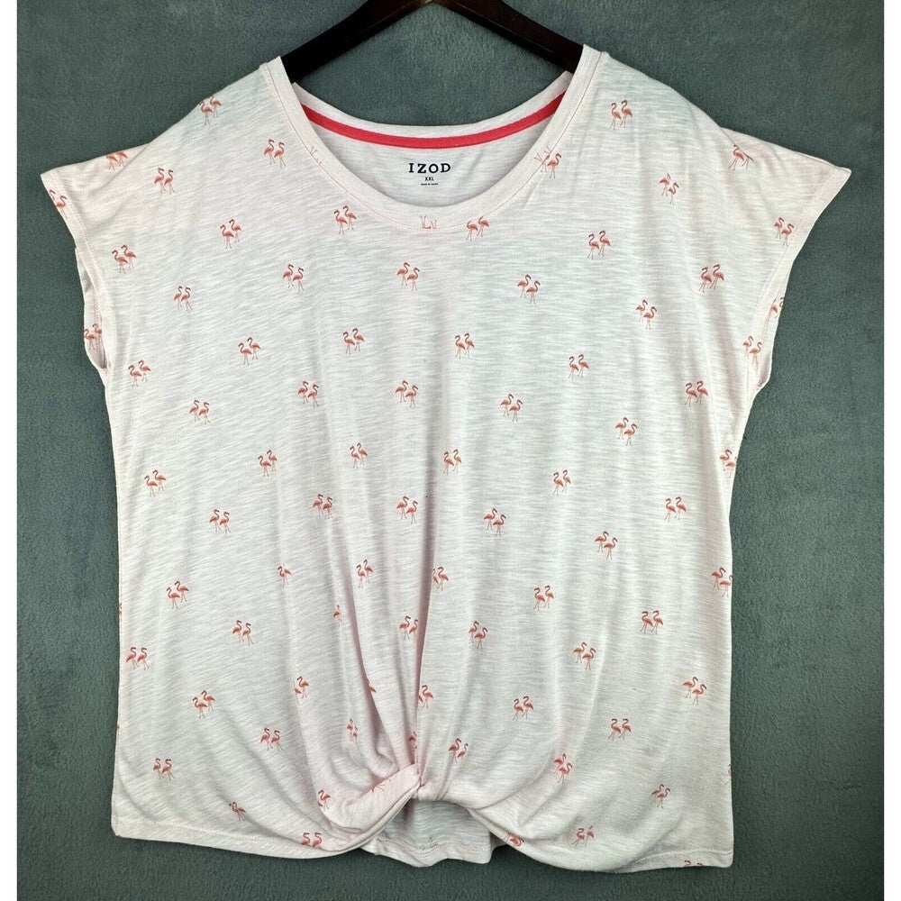 A women's short-sleeve knit top by IZOD, featuring a white heathered base with a small pink and red floral print, a pink inner collar, and a front twist detail, hanging on a dark wooden hanger against a textured gray-green wall.