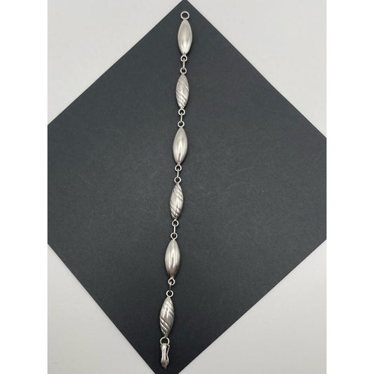 A silver beaded wall hanging or decorative garland with seven elongated textured beads connected by small rings, displayed on a dark gray diamond-shaped card against a light gray background.