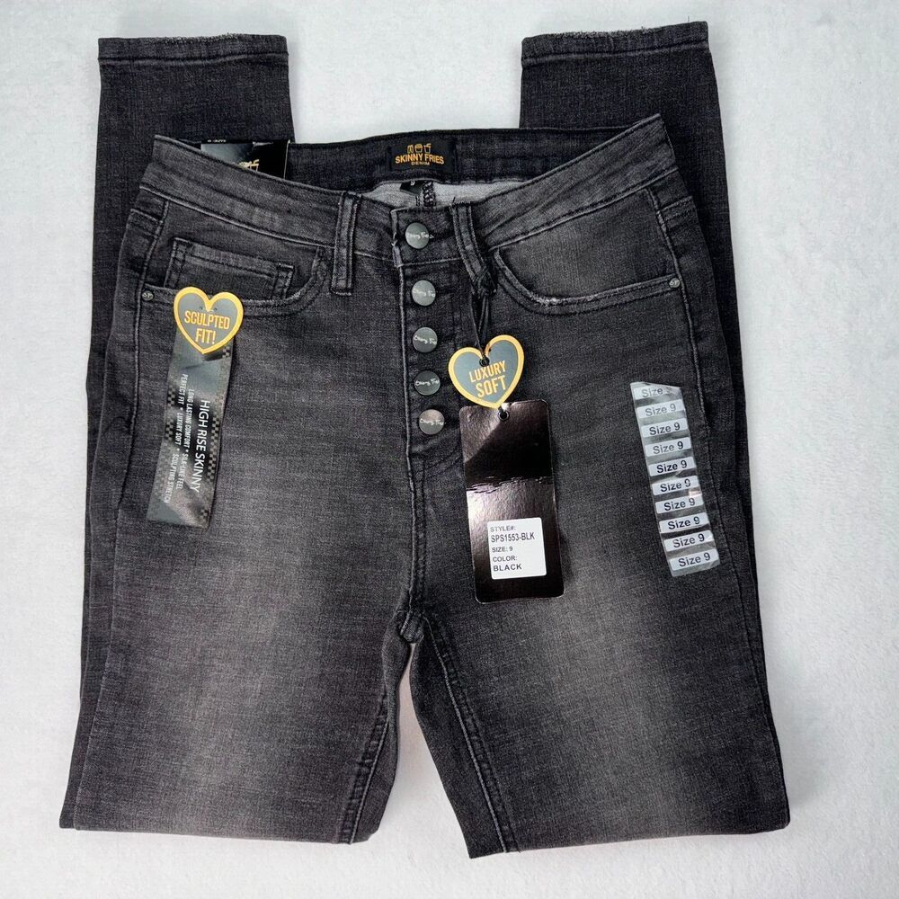 A pair of dark gray washed denim jeans with a unique button-fly front design, featuring decorative gold heart-shaped patches and hang tags, laid flat on a light gray background.