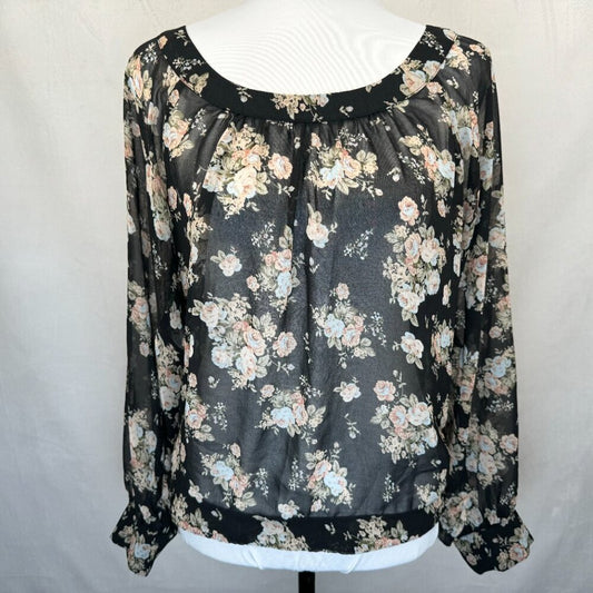 A black sheer long-sleeve blouse with a floral print in pink, beige, and light blue, displayed on a white mannequin torso against a light gray fabric backdrop.