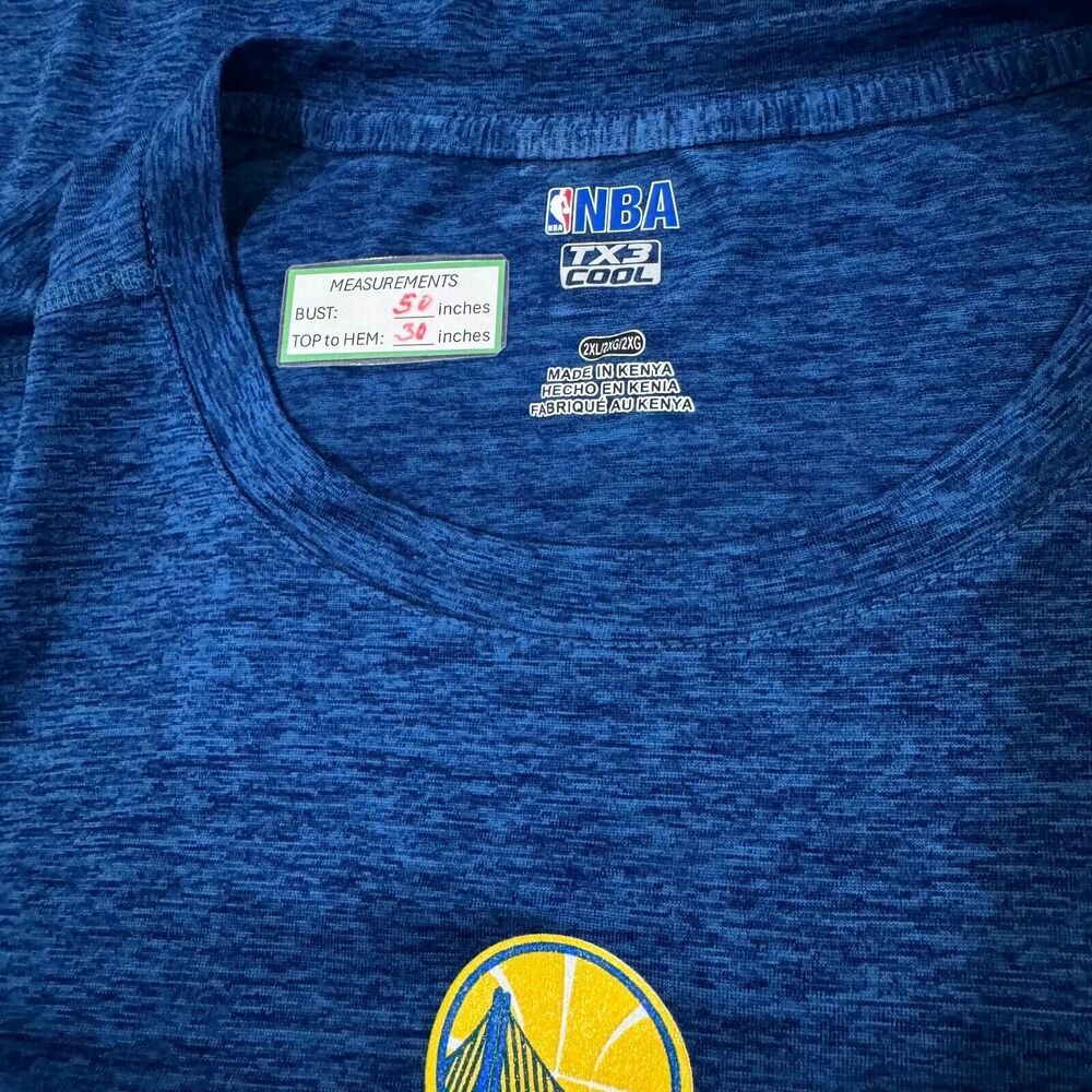 Close-up of a blue heathered NBA T-shirt neck label showing measurements, 1X3 Cool technology, and a Golden State Warriors logo near the bottom.