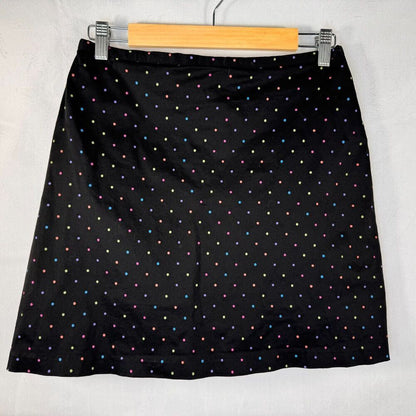 A black A-line skirt with a small multicolor polka dot pattern, hanging on a wooden hanger against a white textured background.