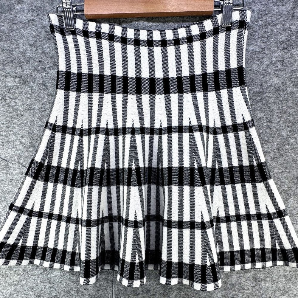 A sleeveless black and white striped pleated skirt hanging from a wooden hanger against a gray textured background.