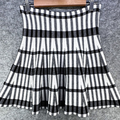 A sleeveless black and white striped pleated skirt hanging from a wooden hanger against a gray textured background.