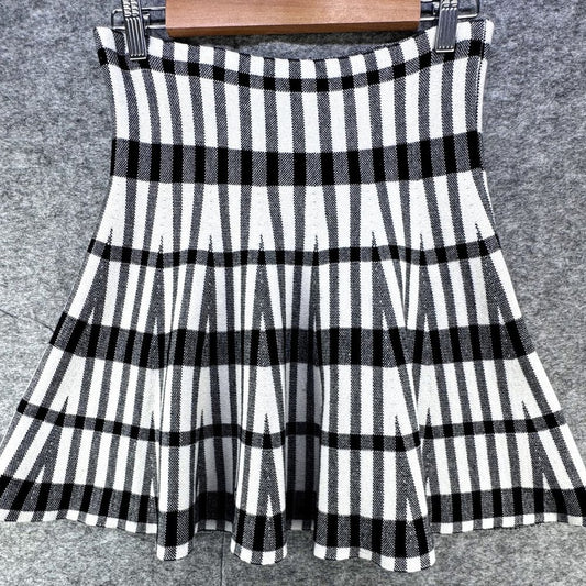 A sleeveless black and white striped pleated skirt hanging from a wooden hanger against a gray textured background.