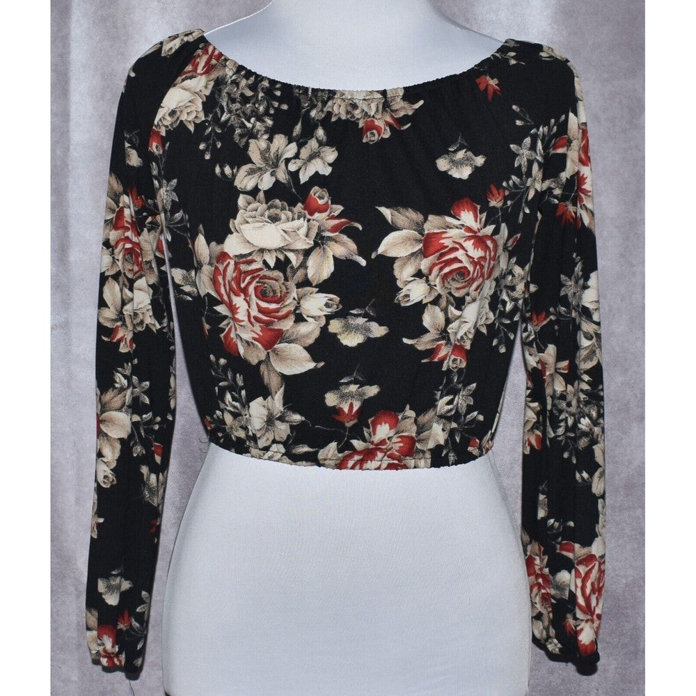 A long-sleeve crop top with a black base and a red, beige, and white floral rose pattern, displayed on a white mannequin torso against a gray textured background.
