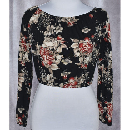 A long-sleeve crop top with a black base and a red, beige, and white floral rose pattern, displayed on a white mannequin torso against a gray textured background.