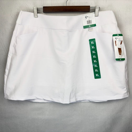 A white high-waisted athletic skirt with side pockets, hanging on a wooden hanger against a gray fabric background. The skirt has retail tags attached, including a green vertical size chart tag showing sizes from S to XL.