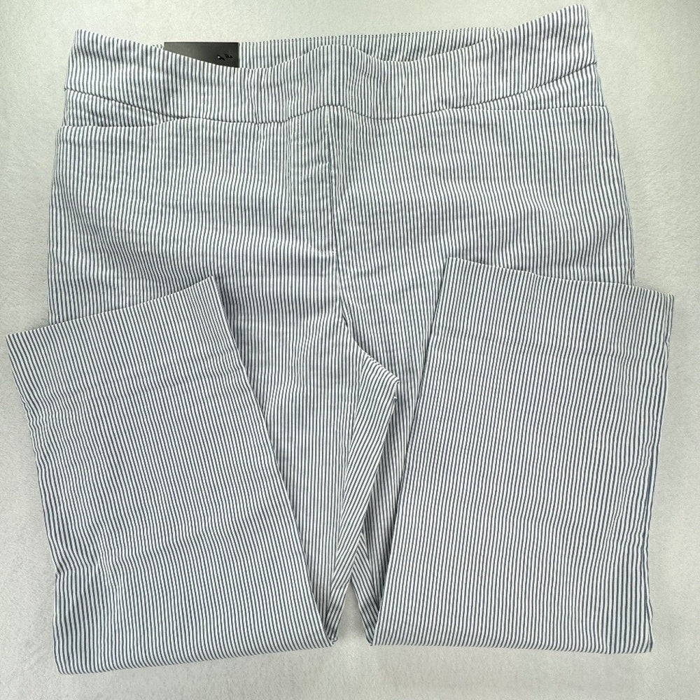 A pair of folded pants with a fine vertical stripe pattern in navy blue and white, laid flat on a light gray background.