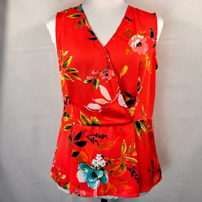 A sleeveless red wrap-style blouse with a vibrant floral print, displayed on a white mannequin torso against a light gray fabric backdrop.