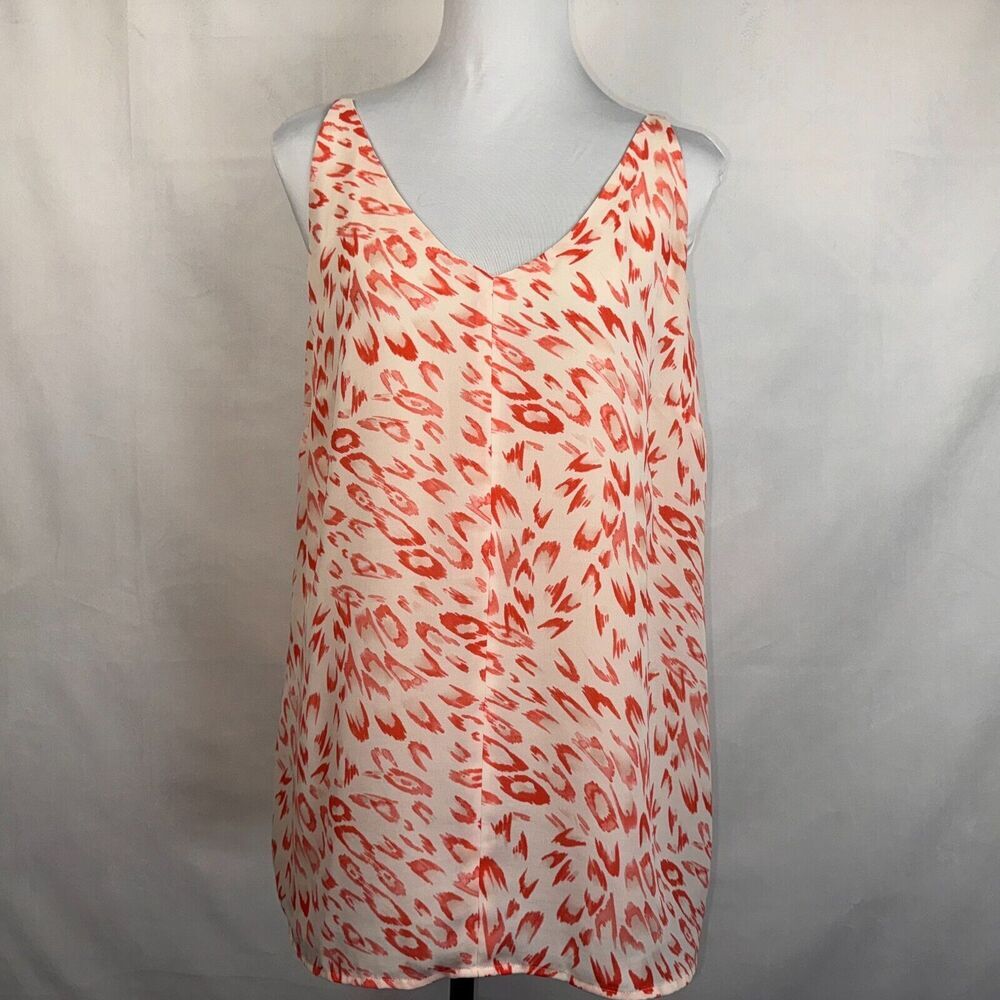 A sleeveless V-neck top with an abstract red and orange brushstroke pattern on a white base, displayed on a gray mannequin torso against a light gray fabric backdrop.