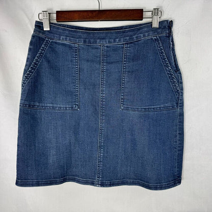 A blue denim mini skirt with front patch pockets, hanging on a wooden hanger against a white fabric background.